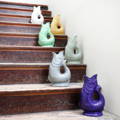Gluggle jugs are in the shape of fishes with the top of the jug being the fish's open mouth and the handle being formed by its tail. This images feature the jugs on a distressed wooden staircase - one on each step. Colours are purple, grey, pale green, pale yellow and white.